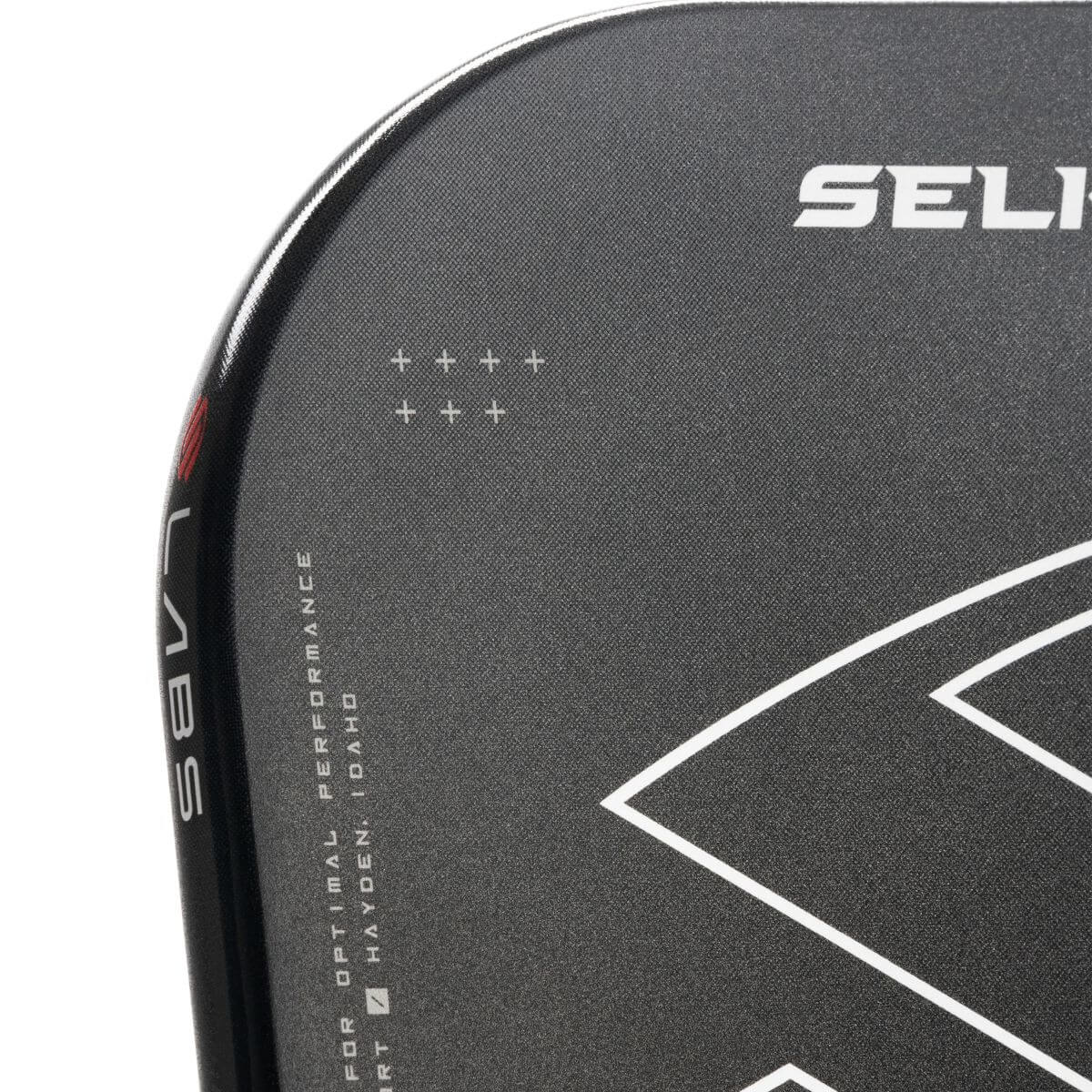 Close-up van de Selkirk LABS 007 Invikta pickleball paddle, zwart blad met rode onderzijde, wit handvat en het Selkirk-logo in zwart met witte omlijning op het slagooppervlak.